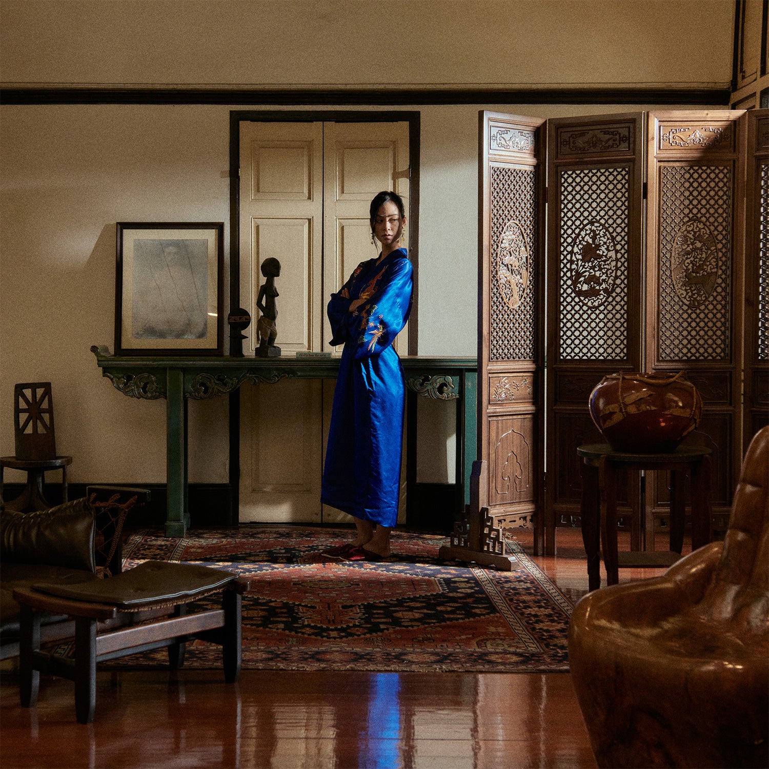 Woman in a blue dress standing in an ornate room with wooden furniture and decorative elements.