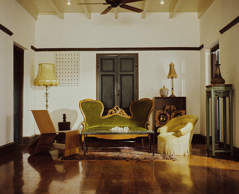 Vintage living room with a velvet green sofa, ornate lamps, and a fringe chair. Dark wooden accents and a cozy, nostalgic ambiance complete the timeless setting.