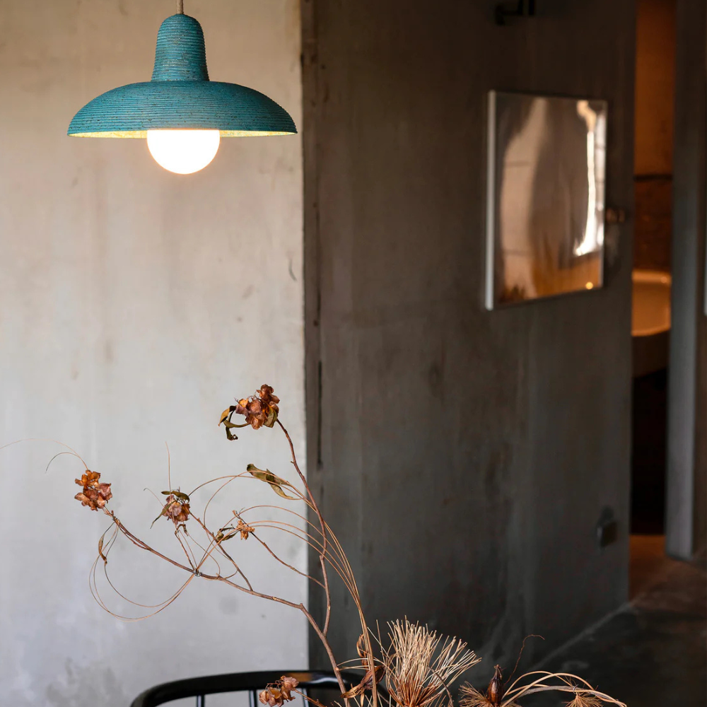 Blue pendant light hanging in a room with a textured wall and decorative plant.