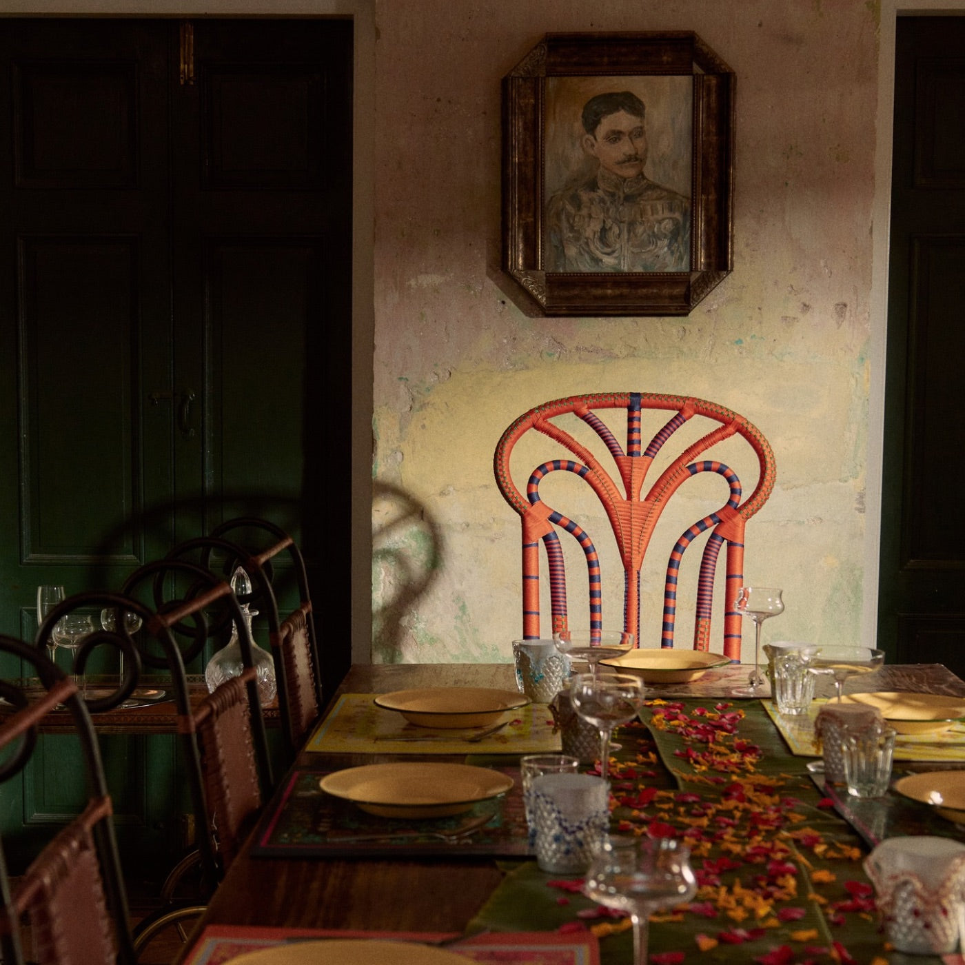 Dining room with a table set for dinner, colorful chair, and portrait on the wall.
